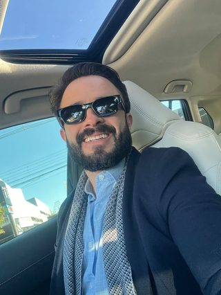Felipe Ramalho sorrindo dentro do carro, em um dia de sol.