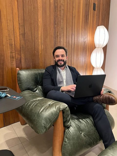 Retrato de Felipe Ramalho sorrindo, sentado com um laptop.